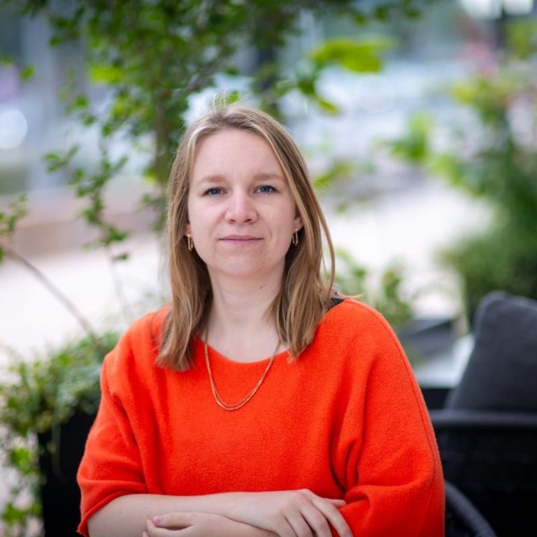 Amelie Haupt - B2B marketing professional with blond hair, wearing bright orange sweater and golden necklace